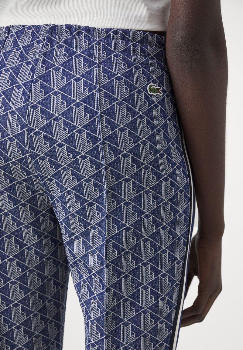 Legginsy w marynarskie wzory z geometrycznym designem i białymi akcentami, elastycznym pasem w talii oraz małą zieloną naszywką po boku.