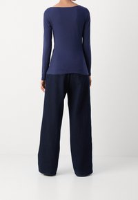 Haut à manches longues bleu marine avec un large col, associé à un pantalon bleu marine ample. Texture lisse avec un tombé subtil.