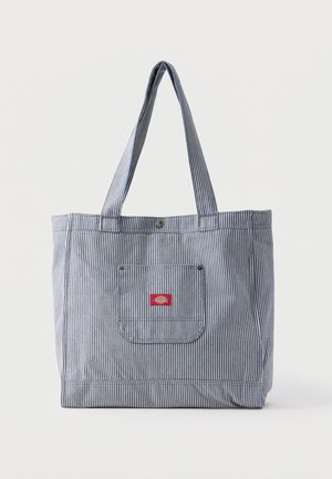 Torba typu tote w niebiesko-białe paski z długimi uchwytami, przednią kieszenią oraz małą czerwoną prostokątną naszywką z logo na kieszeni.