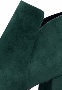 Zelená semišová kotníková bota s blokovým podpatkem, s hladkým povrchem a zakřiveným horním okrajem. Švy podél strany.