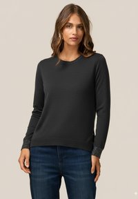 Svart texturerad tröja med långärmar, rund halsringning och glittrande detaljer vid ärmsluten. Kombinerad med mörkblå jeans, enkel design.