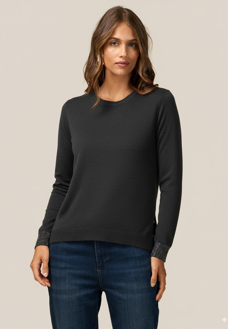 Svart texturerad tröja med långärmar, rund halsringning och glittrande detaljer vid ärmsluten. Kombinerad med mörkblå jeans, enkel design.