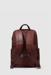 Zaino in pelle marrone con superficie testurizzata, spallacci imbottiti, due tasche laterali e una maniglia superiore per il trasporto.