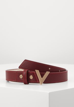 Ceinture en cuir rouge texturé avec une boucle dorée en forme de V, reposant enroulée sur une surface blanche.