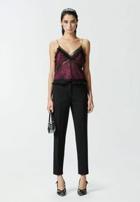 Prozirni ljubičasti leopardići top s crnim čipkastim rubom, uparen sa visokim crnim hlačama i odgovarajućim sandalama s remenčićima. Crna mini torbica.