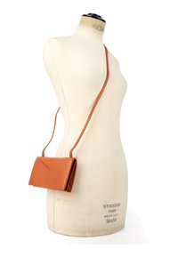 Sac besace en cuir fauve avec fermeture par rabat présenté sur un mannequin de couture couleur crème.