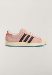 Różowy zamszowy sneaker z czarnymi paskami, kremowym gumowym noskiem i niebieskawą podeszwą. Posiada białe sznurowadła oraz subtelne oznaczenia po bokach.