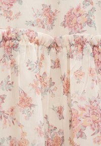 Διαφανές ύφασμα με ροζ και ροδακινί λουλουδένιο σχέδιο, μαζεμένο με ελαστική ραφή.