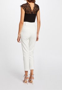 Czarny body z koronkowymi rękawami w kształcie czapki i dekoltem w serek, w połączeniu z białymi dopasowanymi spodniami oraz srebrnymi sandałami na wysokim obcasie.