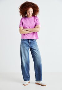 T-shirt rosa a maniche corte con una vestibilità comoda, abbinato a jeans a gamba larga blu chiaro. Sneakers con una base bianca e dettagli grigio chiaro completano il look.