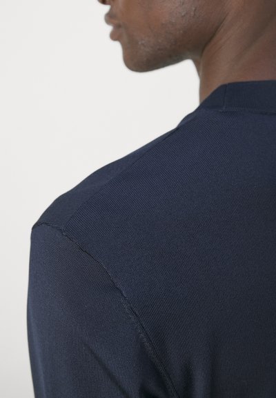 Suéter de punto azul marino con una textura suave, que presenta detalles acanalados en los hombros y un diseño ajustado.