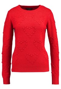 Pull rouge en tricot avec un motif de cœur texturé, col rond et manches longues. Poignets et ourlet côtelés complètent le design.