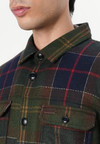 Grün und marineblau kariertes Hemd-Jacke mit wollartiger Textur, mit einer Knopfleiste vorne, Kragen und zwei vorderen Taschen mit schwarzen Knöpfen.