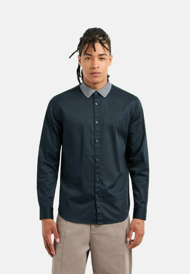 Camicia blu navy con colletto grigio chiaro a contrasto. Maniche lunghe, texture liscia e logo discreto sul petto.