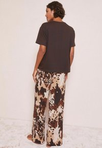 T-shirt marrone a maniche corte abbinato a pantaloni larghi a fantasia con tonalità di marrone e beige, che mostrano un design fluido e rilassato.