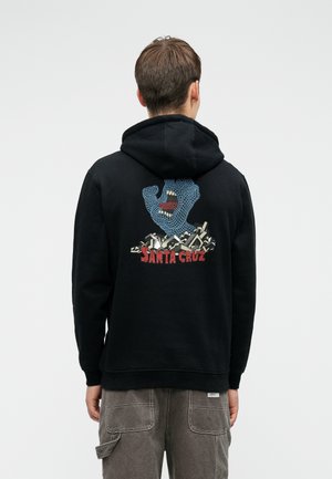 Mustat hupparit, joissa on värikäs grafiikka sinisestä kädestä, jossa on suu, tyyliteltyjen muotojen taustalla, ja "SANTA CRUZ" -teksti alla.