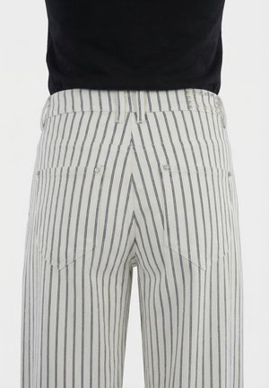 Pantaloni bianchi con sottili strisce verticali nere visti da dietro, con due tasche con rivetti e una cintura con passanti.