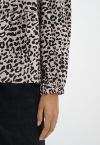  leopardimustriga blouse beeži ja musta värviga, millel on pikad varrukad elastsetega, droonitud disain ja pehme kangakonstruktsioon.