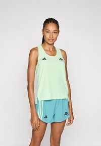 Top deportivo de color verde claro con el logo de Adidas, combinado con pantalones cortos en tono teal. La tela tiene una textura suave y cuenta con aberturas laterales para ventilación.