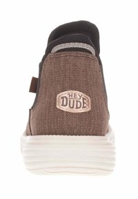 Scarpa slip-on in tela marrone con suola in gomma bianca, caratterizzata da un corpo testurizzato e un logo "HEY DUDE" sul tallone. Accentuata da un bordo nero.