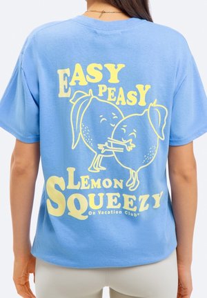 Personne portant un t-shirt bleu avec des citrons jaunes en dessin animé qui s’embrassent et le texte "Easy Peasy Lemon Squeezy" dans le dos.