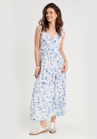 Robe maxi en tissu blanc avec imprimé floral et paysage bleu. Présente un décolleté en V profond, des manches volantées et une jupe évasée à volants.