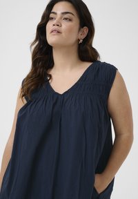Navyblaues ärmelloses Blusenshirt mit V-Ausschnitt, gerafftem Stoff am Oberteil und Seitentaschen. Weiches, leichtes Material mit lockerer Passform.