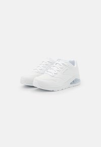Scarpe sportive bianche con tomaia in rete, punta rotonda e dettagli perforati. Presentano una suola ammortizzata con un'unità d'aria trasparente.