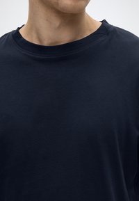 Μπλε ναυτικό βαμβακερό t-shirt με στρογγυλή λαιμόκοψη, κοντά μανίκια και απαλή υφή. Ελάχιστες ραφές και διακριτικές σχεδιαστικές λεπτομέρειες.