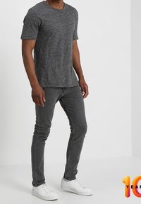 Camiseta gris de manga corta con cuello redondo, combinada con unos jeans gris ajustados y zapatillas blancas. Textura de tela suave y diseño sencillo.