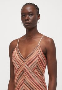 Sleeveless dress featuring a chevron pattern in warm tones of orange, pink, and brown with a V-neck and thin, adjustable straps.