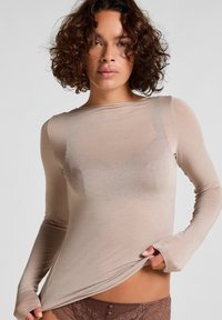 Langsleeve, lichtbeige, aansluitend top van doorschijnend materiaal. Zachte textuur met een ronde halslijn en verlengde mouwen.
