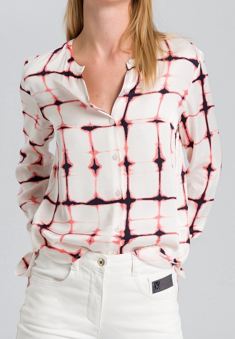 Chemise à boutons en tissu léger avec un motif à carreaux rose et noir sur un fond crème. Manches longues et col à revers.