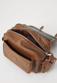 La borsa in pelle marrone presenta un motivo inciso intricato, due scomparti con zip e una tasca frontale. Gli accenti includono hardware in argento.