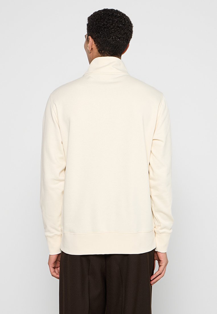 Cremfarbener Pullover mit hohem Kragen, langen Ärmeln und gerippten Bündchen. Weicher Stoff und schlichtes Design ohne sichtbare Muster.