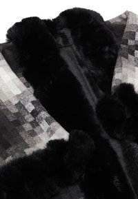 Wrap griș și negru cu un model cu blană sintetică neagră pufoasă pe margini, având un amestec de modele geometrice și texturi.