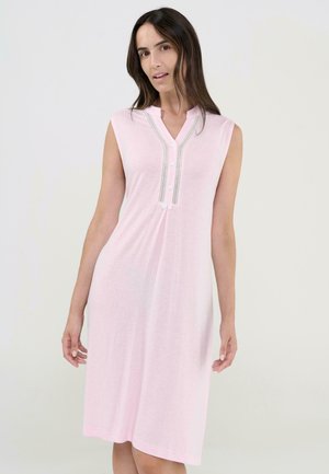 Mujer vistiendo un vestido sin mangas de color rosa claro hasta la rodilla, con escote abotonado y ribete de encaje, de pie frente a un fondo liso.