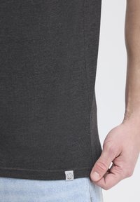Camiseta gris oscuro hecha de una tela suave, con una etiqueta en el dobladillo inferior. Diseño ajustado con una textura lisa y un acabado limpio.