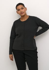 Dunkelgraue gerippte Strickjacke mit Rundhalsausschnitt, Knöpfen vorne und langen Ärmeln, kombiniert mit schwarzen Hosen. Glatte Textur mit taillierter Passform.