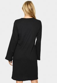Svart klänning med lång ärm och avslappnad passform, tillverkad av ett något strukturerat tyg. Har en rund halsringning och slutar ovanför knät.