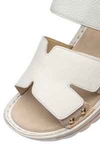 White leather sandal with wide cut-out strap, beige cushioned footbed, and two gold rivets near the sole edge.