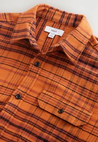 Oranje geruite flanellen shirt met zwarte lijnen, knoopsluiting en een enkele borstzak; zachte textuur en middelmatig zware stof.