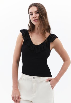 Zwarte tanktop met een kanten ruchehalslijn en schouderaccenten, aansluitende silhoët, gedragen met lichte broeken. Glad textuur.