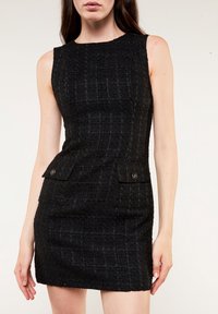 Abito nero senza maniche con un tessuto strutturato, caratterizzato da una silhouette aderente e due tasche frontali con bottoni.
