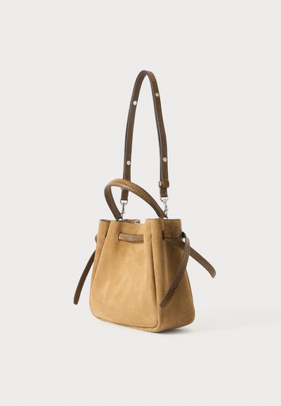 Sac à main en daim beige doux avec des poignées en cuir marron foncé texturé et une sangle d'épaule réglable sur un fond clair uni.