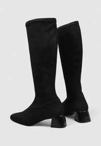 Black knee-high boots made of soft suede. They feature a pointed toe and a chunky, square heel for stability. Smooth finish with a seamless design.