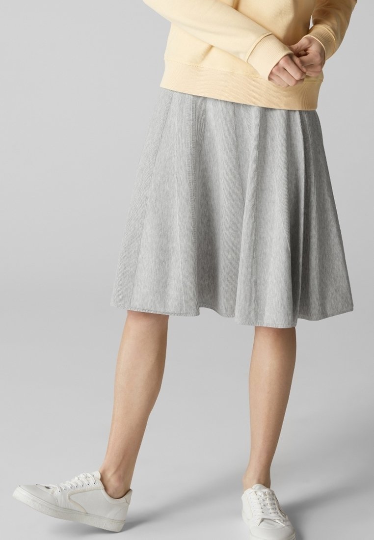 Jupe grise longueur genou en ligne A avec texture côtelée verticale, associée à des baskets blanches et un pull jaune clair.