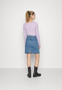 Blusa lilás de mangas compridas com corte reto, combinada com uma saia de ganga com uma racha nas costas e bolsos laterais, complementada por botins pretos.