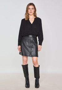 Blusa nera con bottoni a v e maniche lunghe abbinata a una gonna nera in pelle svasata con chiusura frontale a bottoni e finitura testurizzata.