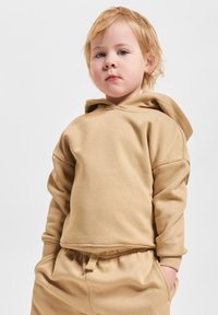 Sudadera con capucha de color marrón, hecha de una tela suave, con mangas largas, un corte relajado y un bolsillo tipo canguro. Combinada con pantalones jogger a juego.